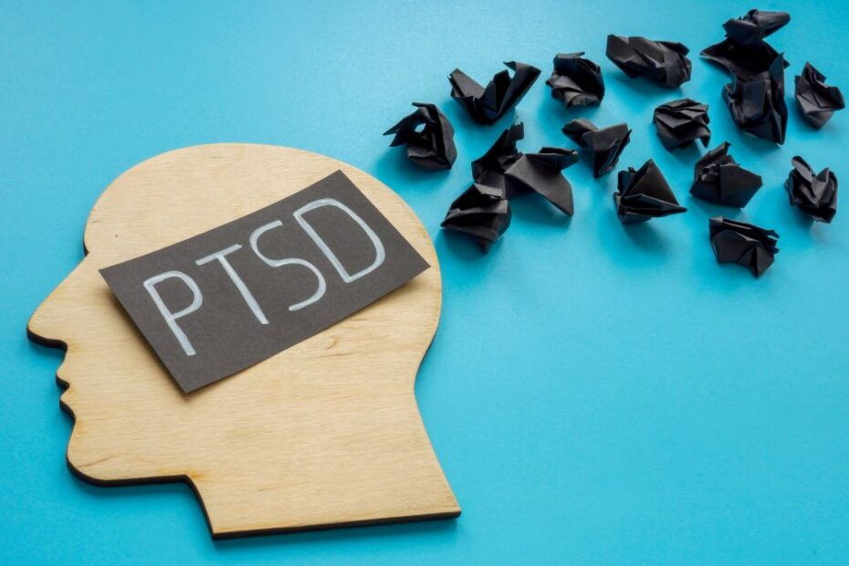 Illustration du syndrome de stress post-traumatique (PTSD) avec une silhouette de tête en bois et des papiers froissés noirs représentant des pensées négatives.